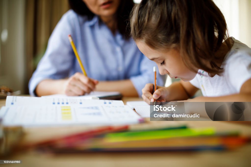 A student is engaged in writing in a book at a library, surrounded by numerous books, reflecting a studious atmosphere